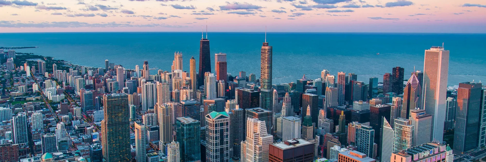 Bird's eye view of the Chicago skyline at sundown with water and clouds in the background.